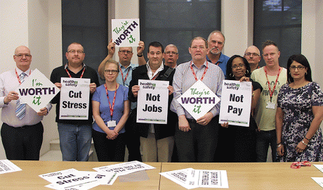 Members of the health and safety committee holding boards reading 'cut stress, not jobs, not pay'