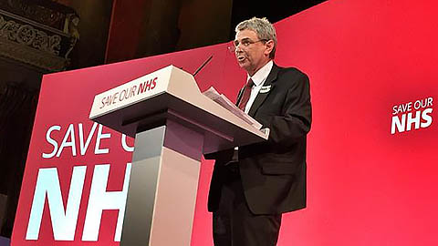 Dave Prentis at rostrum in front of Save Our NHS backdrop