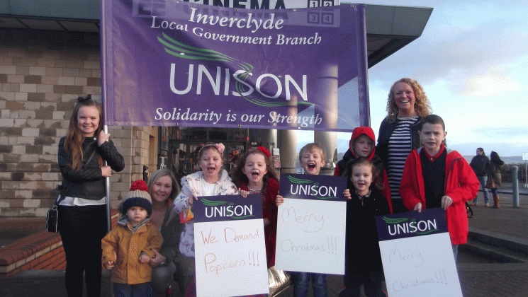 Children attending UNISON's Christmas cinema screening in Inverclyde stand outside the cinema holding placards saying 'we demand popcorn'