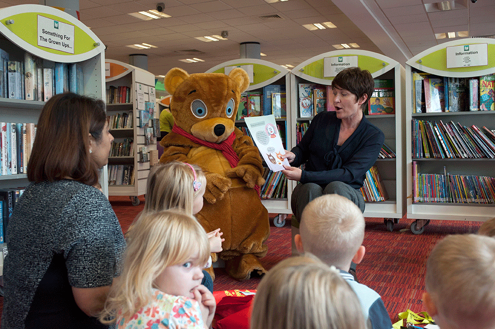 Library worker Shazzia Rock reads to children with Woody the bear
