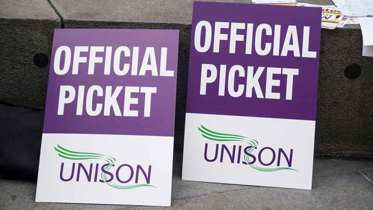 Two placards, the top is purple with the words 'OFFICIAL PICKET' in white capital letters, and the bottom half is white, with the UNISON logo on