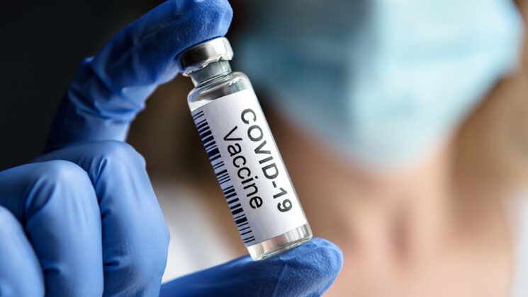 Gloved hand holding vial of COVID-19 vaccine