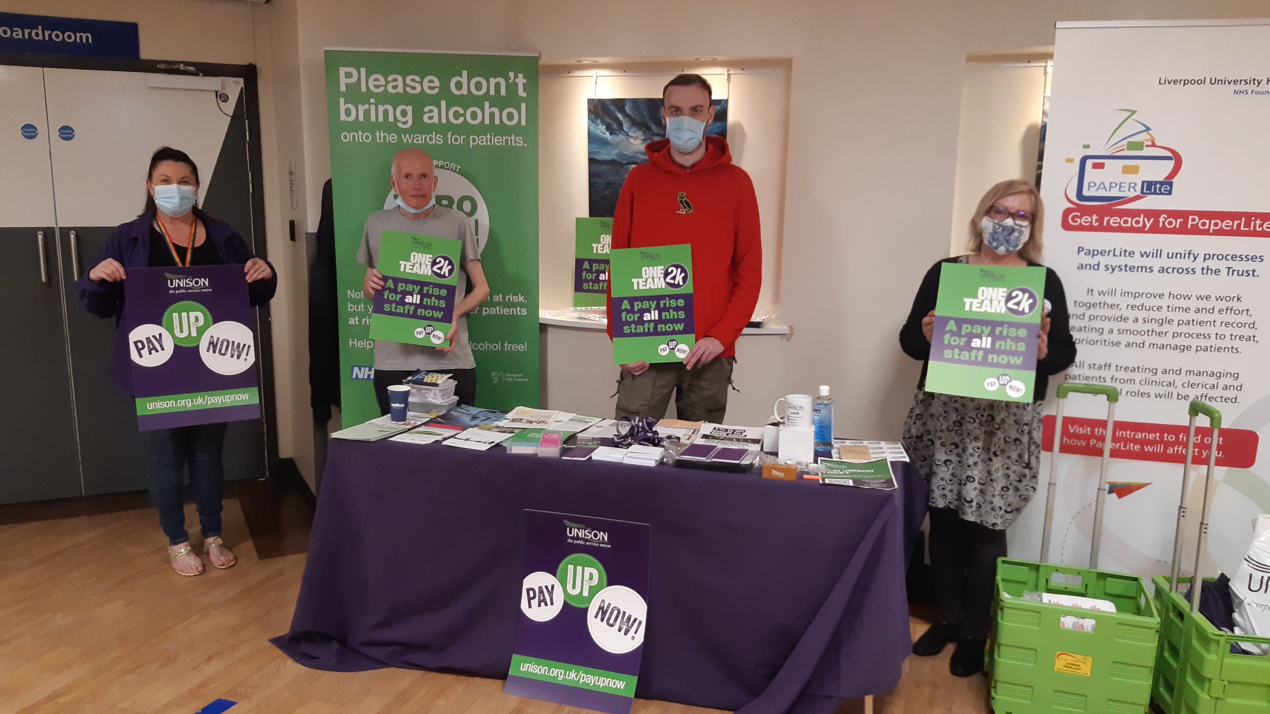 Hospital staff standing by a table with signs saying 'pay up now'