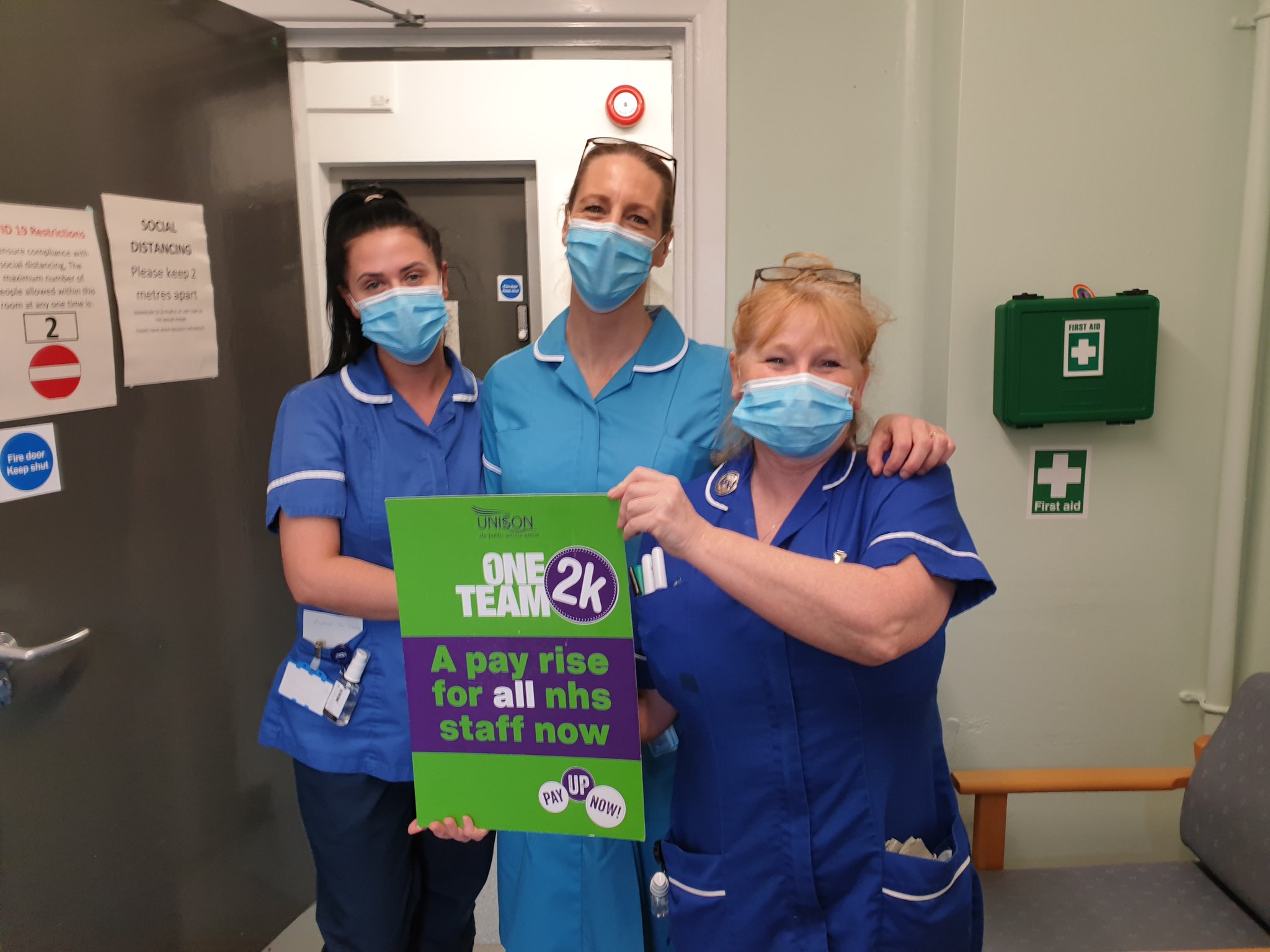 Three female nurses behind sign that says 'a pay rise for all NHS staff'