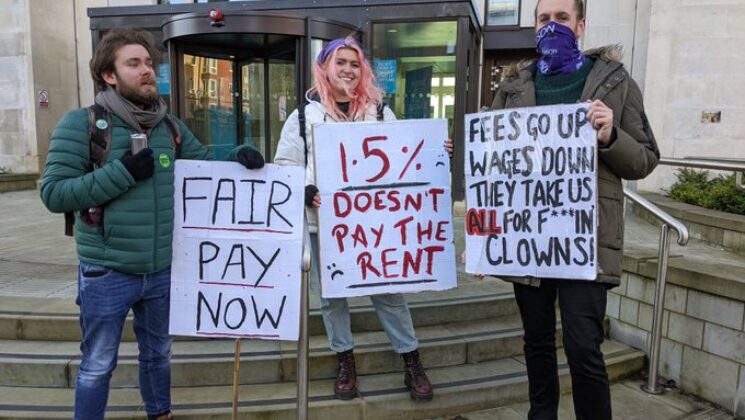 Workers on the picket line in Leeds, with placards that say 'Fair pay now' and '1.5% doesn't pay the rent'