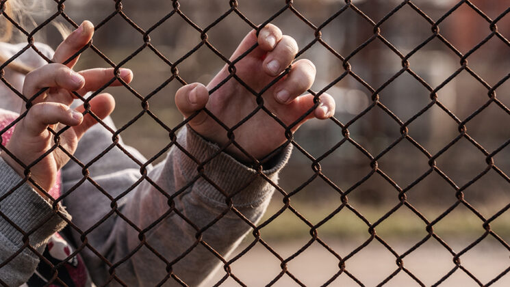 A child refugees hands on a wire fence