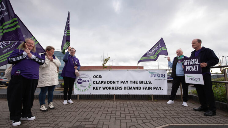Five UNISON members on an OCS picket line, with UNISON flags and banner reading: 'Claps don't pay the bills – key workers demand fair pay'.