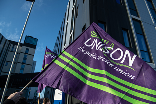 A UNISON flag waving against a blue sky outside The Royal Liverpool University Hospital, Liverpool, UK