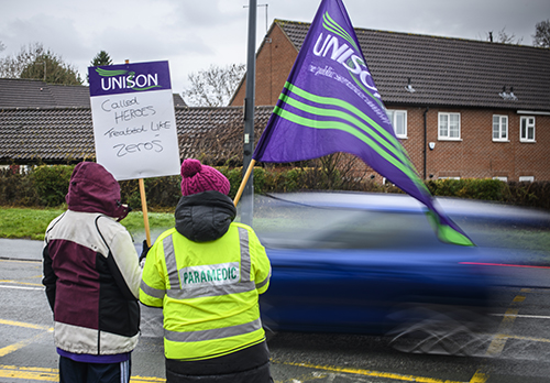 Two pickets, with placard and flag, waving at a passing car, which is blurred by its speed