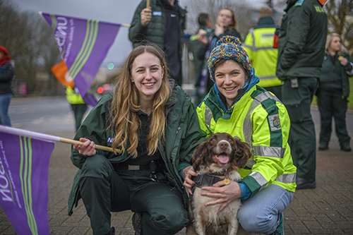 Two women on a picket line with a dog, and UNISON banners in the background.