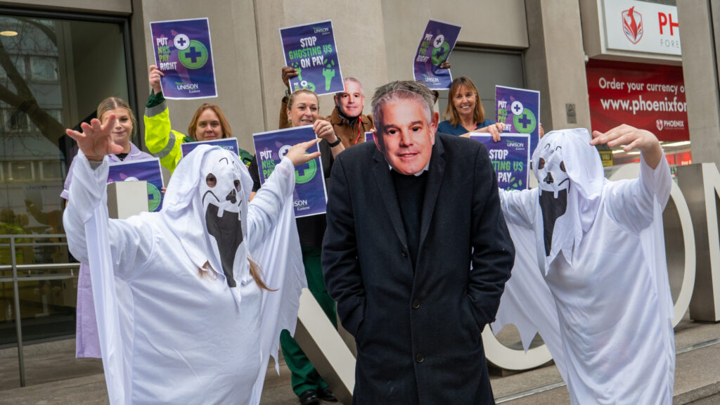 A person in a Steve Barclay mask is surrounded by people dressed as ghosts. 