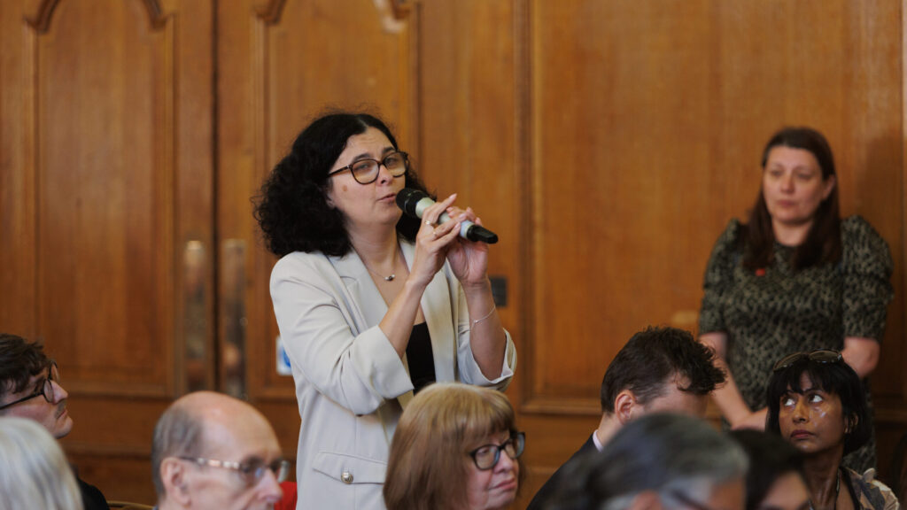 An audience member at the launch of support guarenteed, holding a microphone, asks a question of the panel